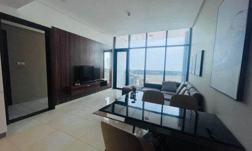 A luxury living room with a large window overlooking the ocean in a 1 BR apartment located in Juffair.