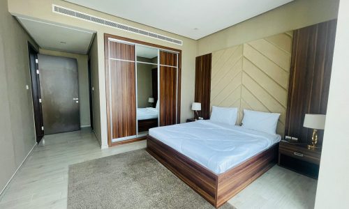 A luxury 1 BR apartment in Juffair with a bed, dresser and mirror.