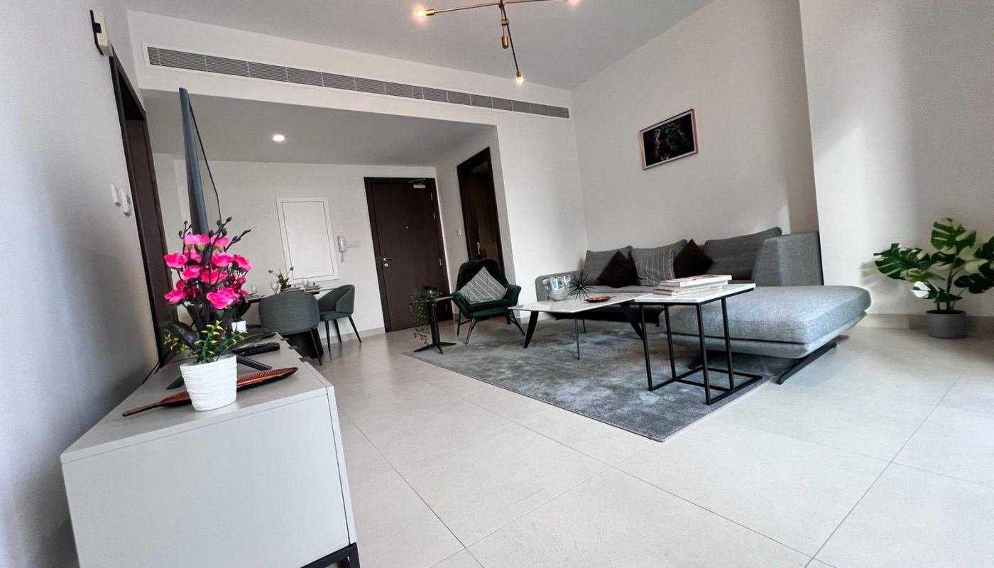 A luxury living room in a Juffair 1BR apartment with a white couch and TV.