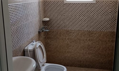 A bathroom with a toilet, sink and drafty window.