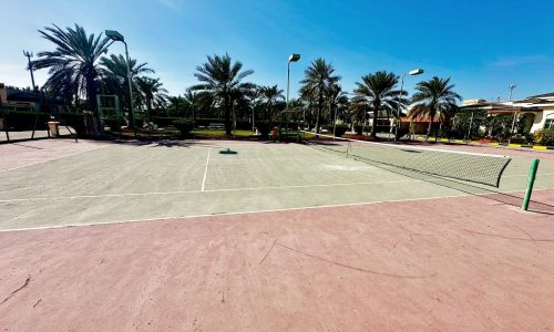 A two-story villa with a tennis court and palm trees in the background.