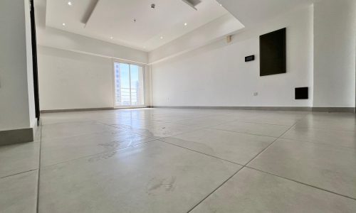 An empty apartment with white tile floors and a large window for sale in Juffair.