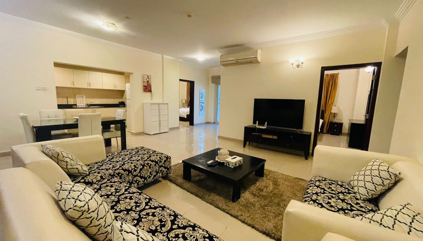 A living room in a 2BR apartment with a couch, coffee table, and TV.