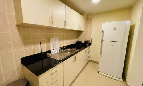 A small kitchen with a refrigerator and microwave in a 2BR apartment in Juffair.