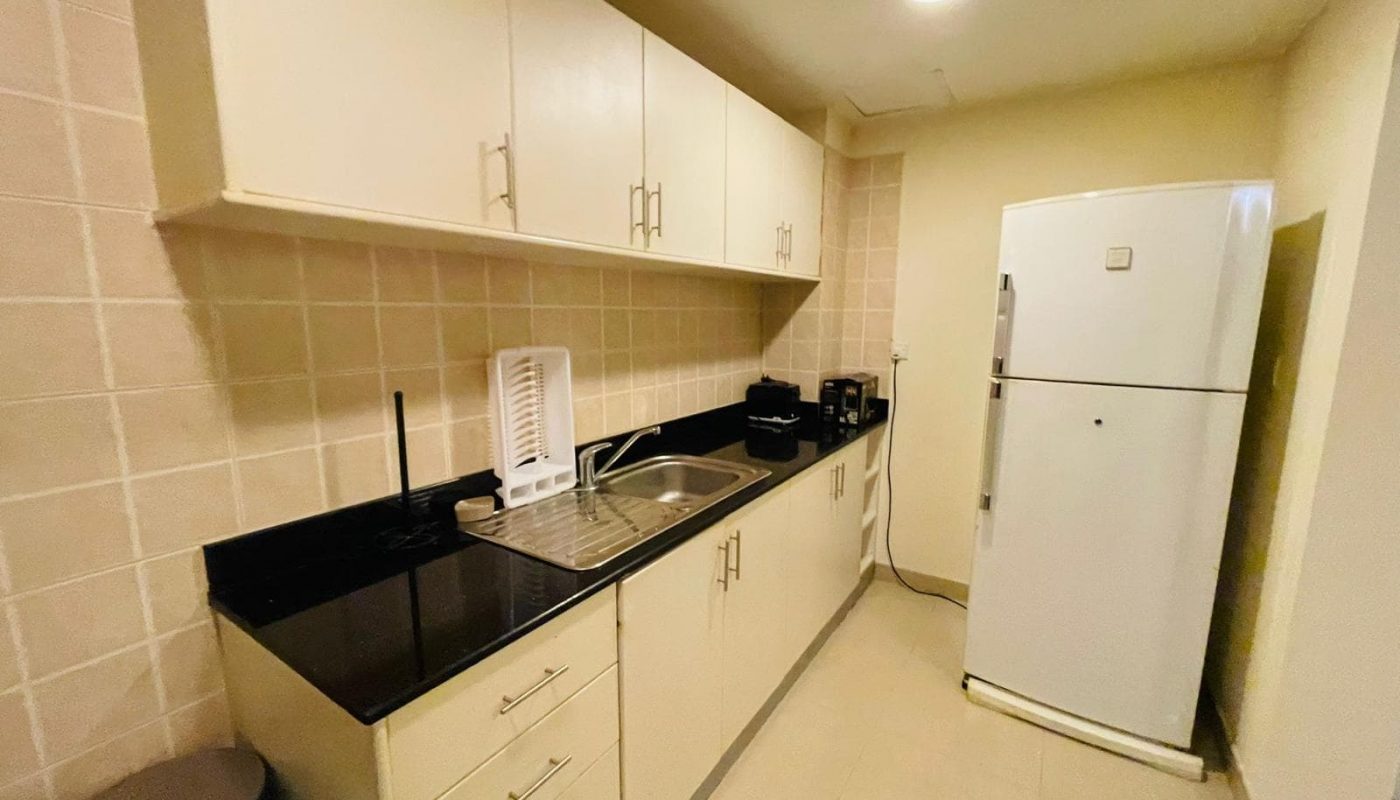 A small kitchen with a refrigerator and microwave in a 2BR apartment in Juffair.
