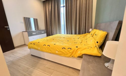 A bed with yellow sheets and a lamp next to a dresser in an auto-themed bedroom.