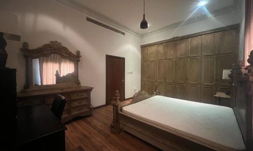 A JUFAAIR bedroom with a bed, dresser and mirror available for rent in a villa.