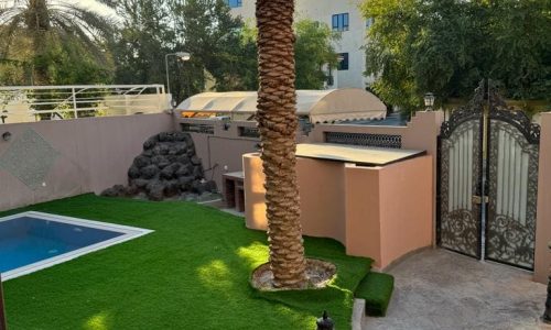 A villa for rent in Juffair with a backyard adorned with artificial grass and a palm tree.