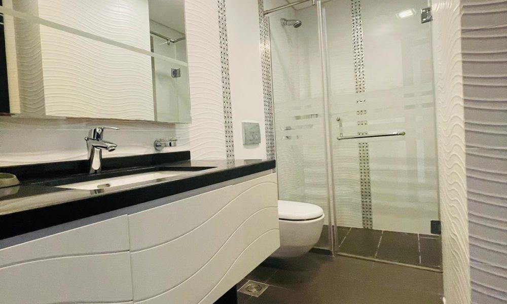 A luxury white and black bathroom with a sink and mirror in a Seef 1BR Apartment.