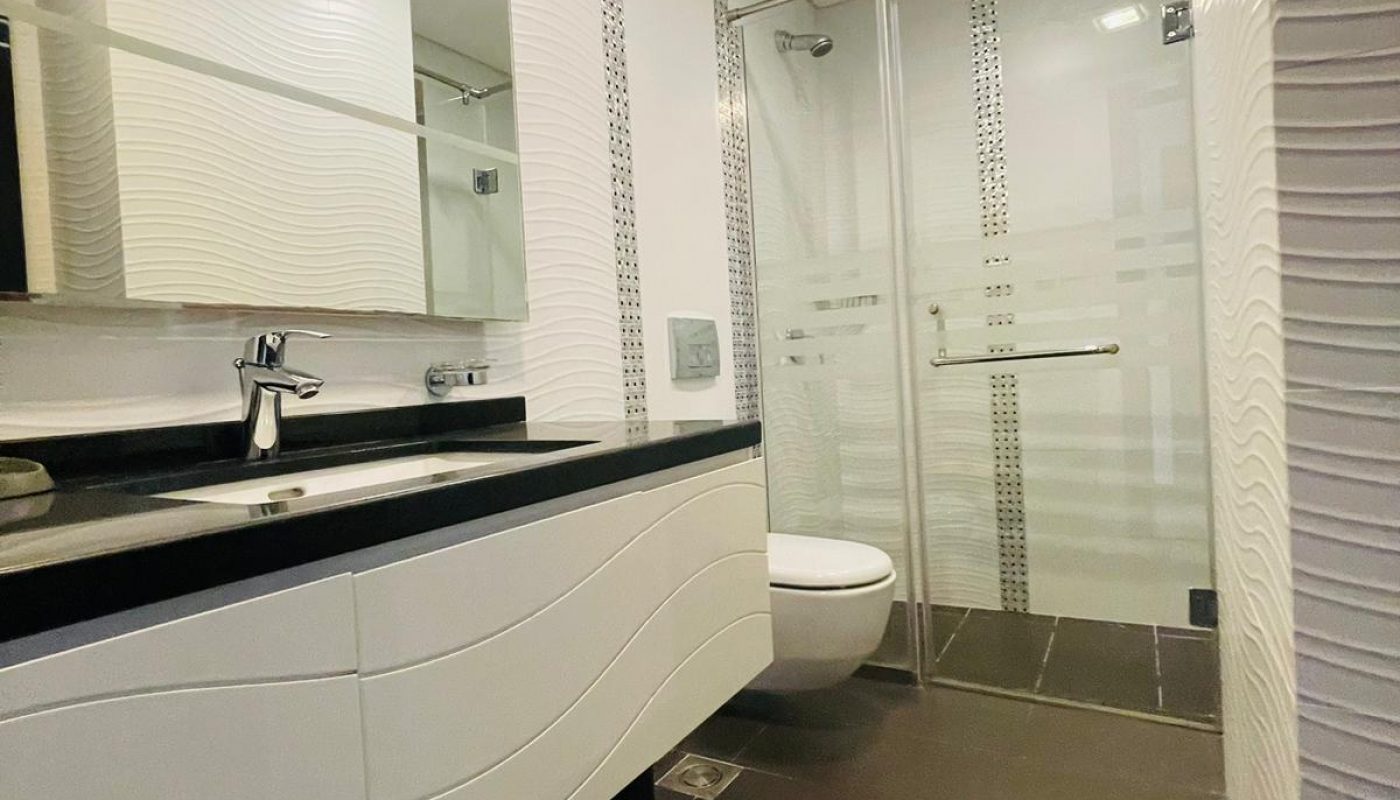A luxury white and black bathroom with a sink and mirror in a Seef 1BR Apartment.