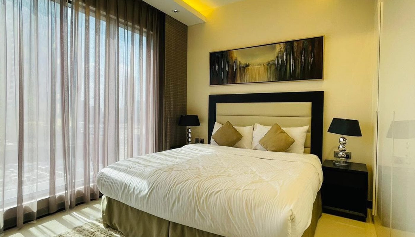 A luxury bedroom with a white bed and yellow lighting in a Seef 1BR apartment.