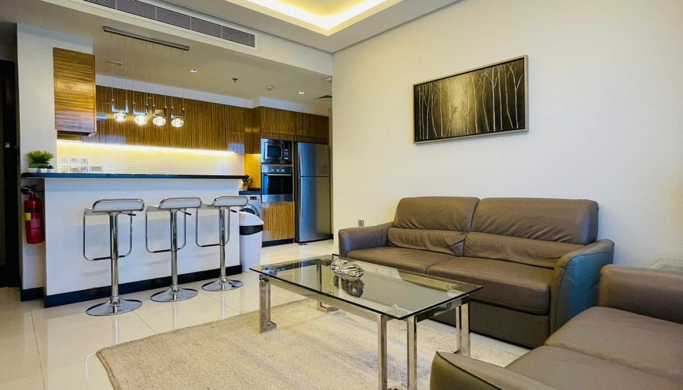 A modern living room and kitchen area in a luxurious 1BR apartment located in Seef.