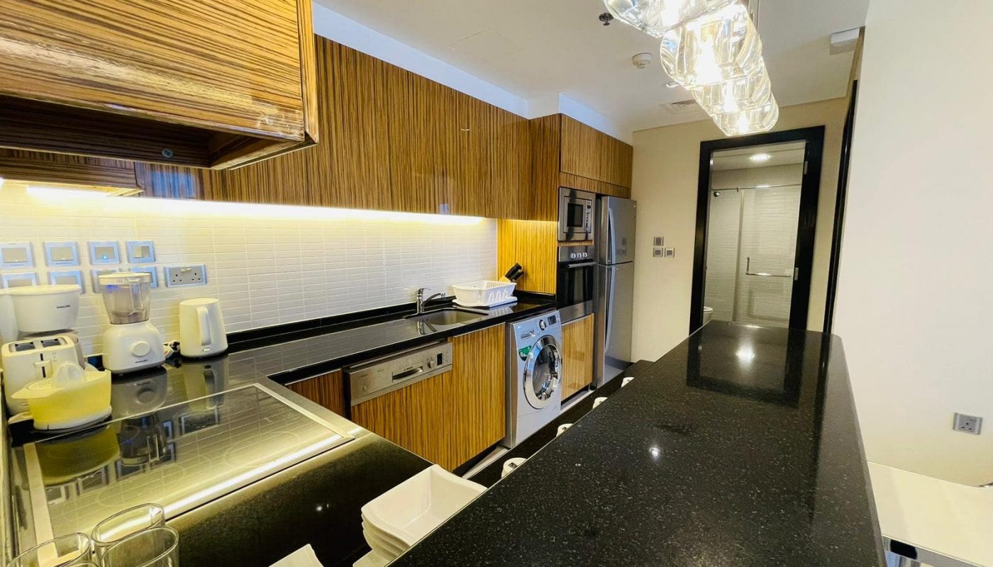 A luxury 1BR apartment in Seef with a kitchenette featuring black counter tops and stainless steel appliances.