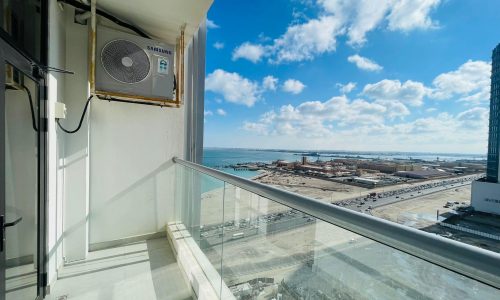 A spacious and modern living balcony with a view of the ocean and city.