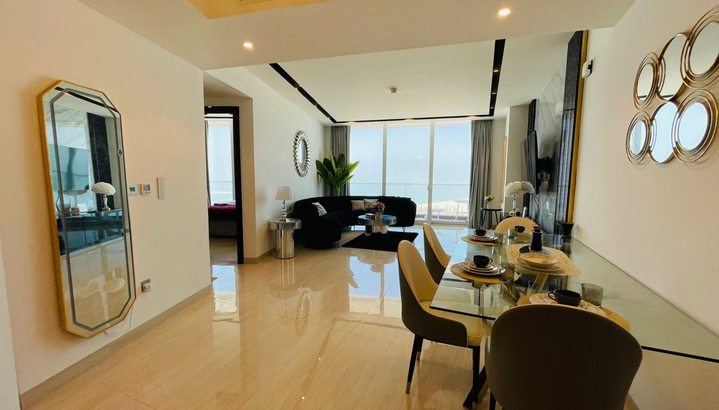 A living room with a dining table and chairs and a view of the ocean.