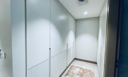 A hallway with white cabinets and a rug.