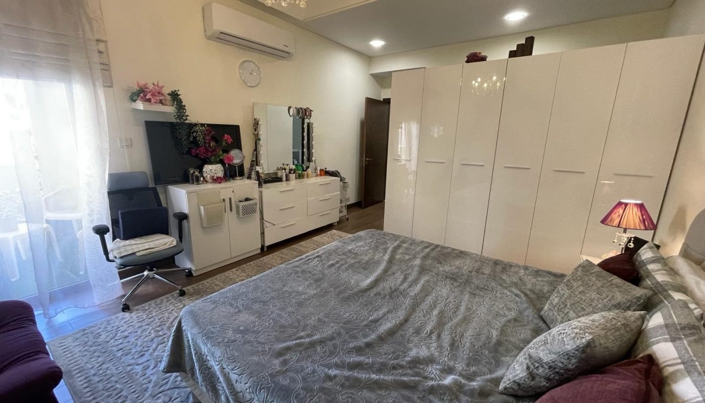 A furnished bedroom in Danat Isa Town apartment, equipped with a bed, dresser, and TV.