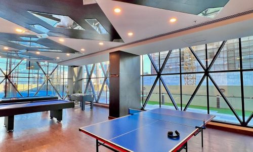 A modern office recreation room with a ping pong table, hardwood floors, and angular skylights.