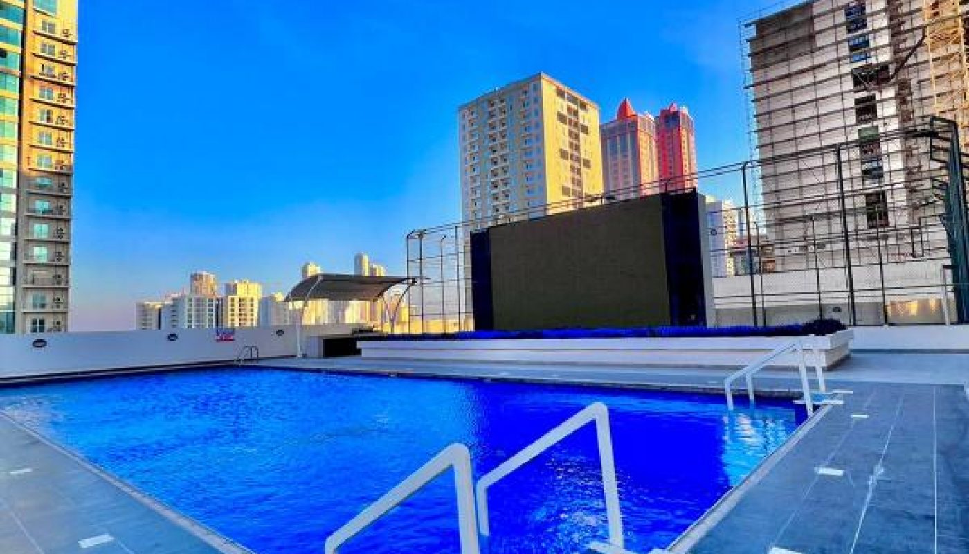 Rooftop swimming pool with clear blue water, surrounded by tall city buildings and a construction site under a bright blue sky.