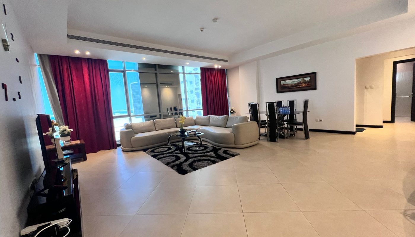 Spacious living and dining area with tiled floor, beige sectional sofa, black rug, glass coffee table, dining table, large window, and maroon curtains.