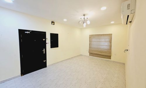 For rent: Spacious, empty apartment with tiled flooring, white walls, air conditioning unit, and a closed garage door.