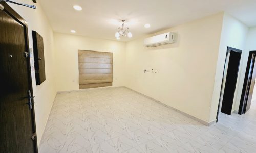 Apartment for rent: Empty room with white tiled flooring, off-white walls, one air conditioner, and ceiling lights in Saar.