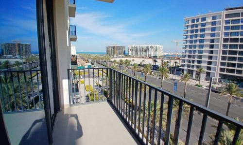 Balcony view of a coastal city with high-rise buildings, the MG Mall, and clear blue skies.