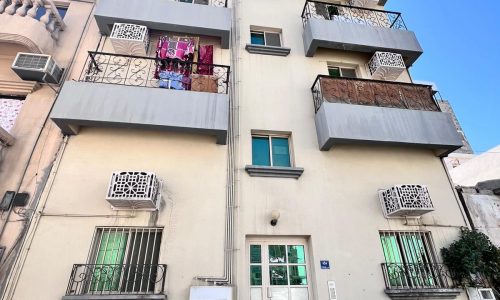 Apartment building facade with balconies, some adorned with hanging laundry, on a clear day.