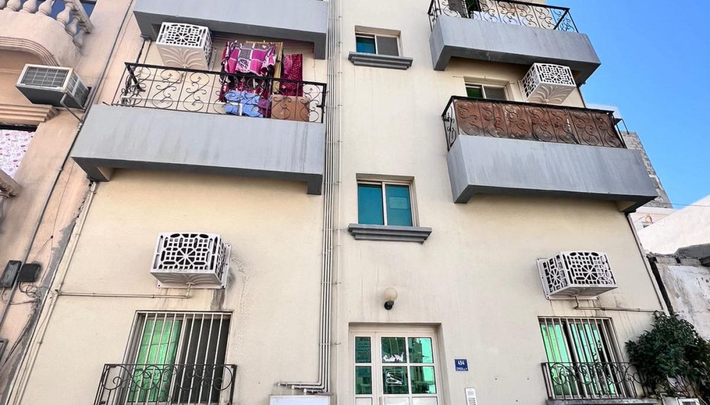 Apartment building facade with balconies, some adorned with hanging laundry, on a clear day.