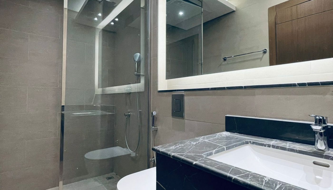 Modern bathroom with a glass-enclosed shower, wall-mounted toilet, large mirror, and black marble sink countertop under recessed ceiling lights.