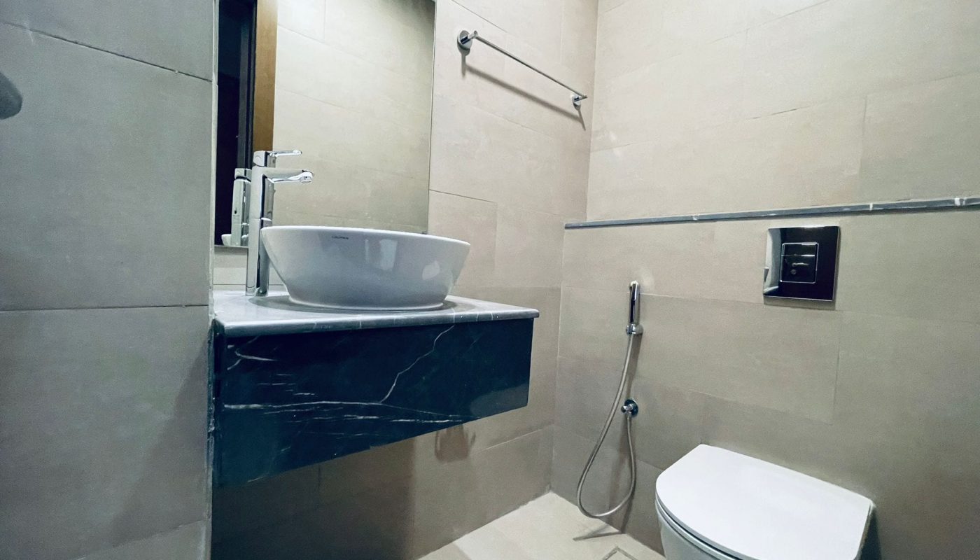 Modern bathroom interior in a 1BR apartment with an eye-catching wall-mounted sink, toilet, and handheld shower in Juffair.
