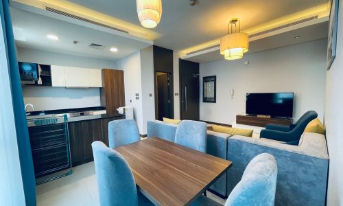 Amazing apartment interior with an open-plan kitchen and dining area, featuring a wooden dining table, blue upholstered chairs, and pendant lighting.