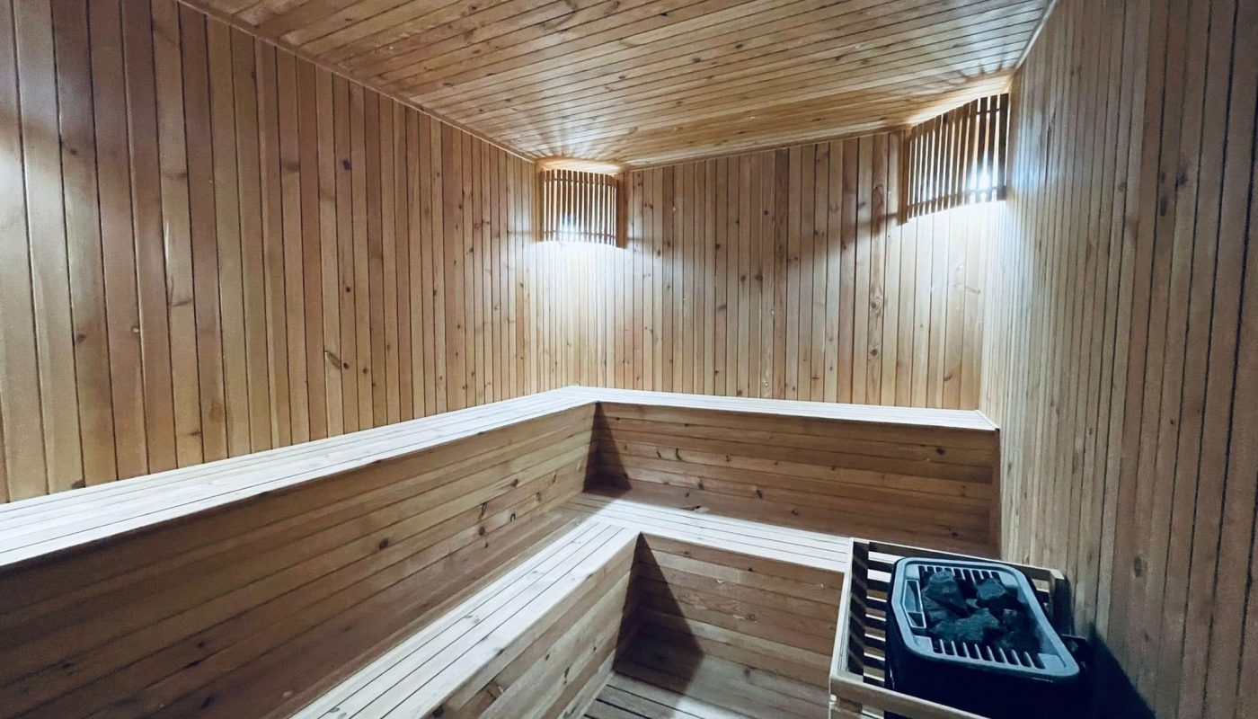 Interior of a wooden sauna room with benches and an eye-catching electric heater in a 1BR apartment.
