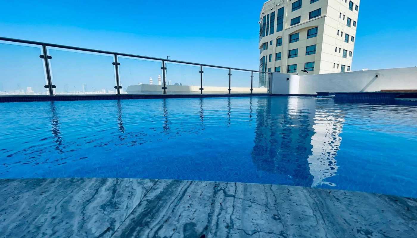Apartment for rent with an amazing rooftop swimming pool featuring clear blue water overlooking a cityscape under a bright blue sky in Juffair.