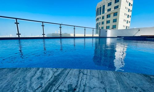 Rooftop swimming pool with a clear blue sky, overlooking an eye-catching urban building in Juffair.