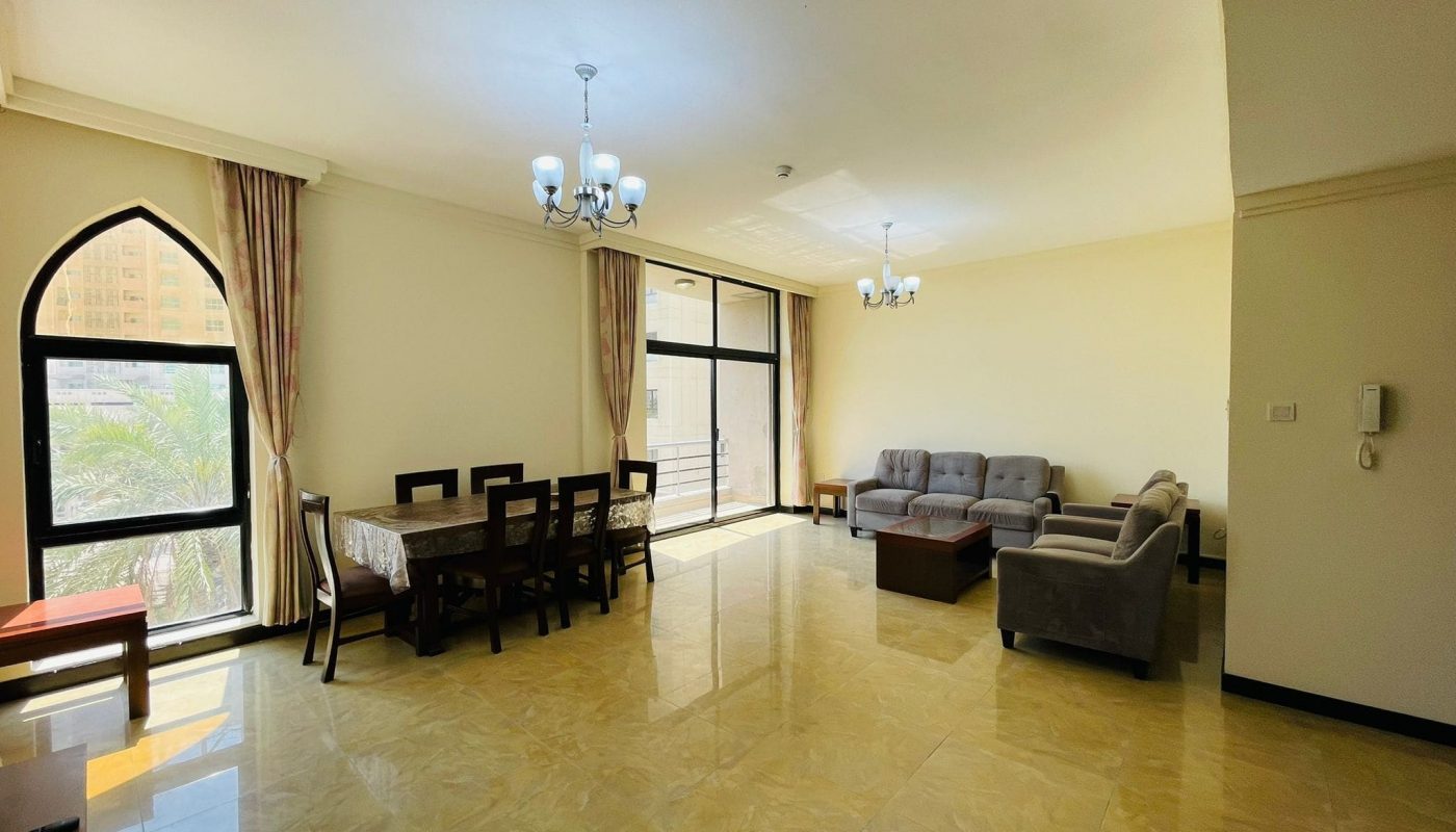 Spacious living room with dining area, large windows, and contemporary furniture in a Juffair apartment for rent.