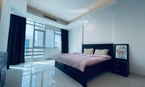 Modern bedroom with a dark wood bed and furniture, light walls, and glossy tile flooring.