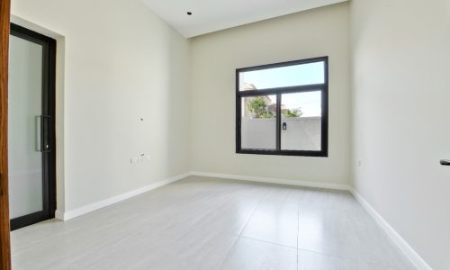 A clean, empty room with a large window, beige walls, and gray flooring awaits its auto draft.