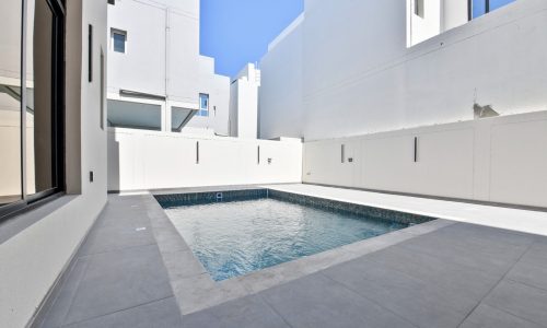 A small rectangular pool in a modern, minimalist white courtyard with grey flooring.