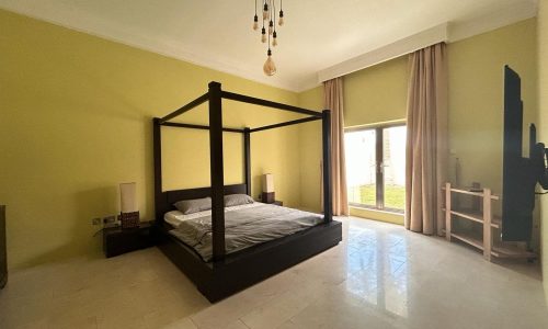 A spacious bedroom within a compound villa, featuring a four-poster bed, pale yellow walls, and a large window with curtains in the Hamala Area.