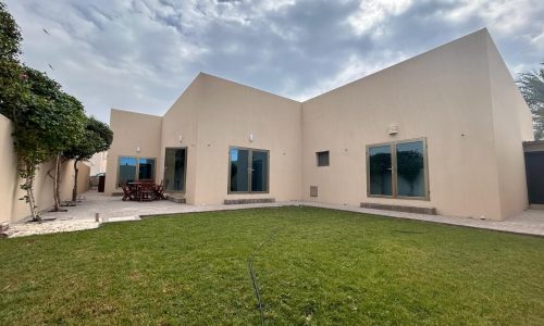 A single-story villa for rent in the Compound Hamala Area, with a beige exterior and a small garden area with a lawn and outdoor seating.