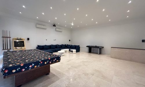 An empty room in a Villa for Rent in Compound Hamala, with a pool table, seating area, air conditioning unit, and a jukebox.