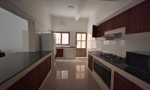 Modern kitchen interior in a Villa for rent in Budaiya, featuring wooden cabinets and stainless steel appliances.