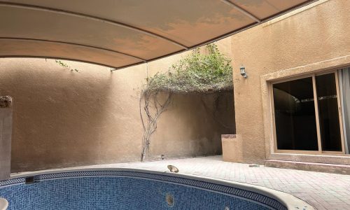 A semi-enclosed outdoor space within the Compound Budaiya, featuring a curved pool and a climbing plant on the wall.