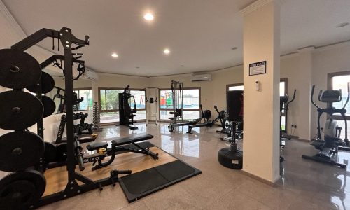 A well-equipped indoor gym with various workout machines and weights in a villa for rent, located in the Budaiya area.