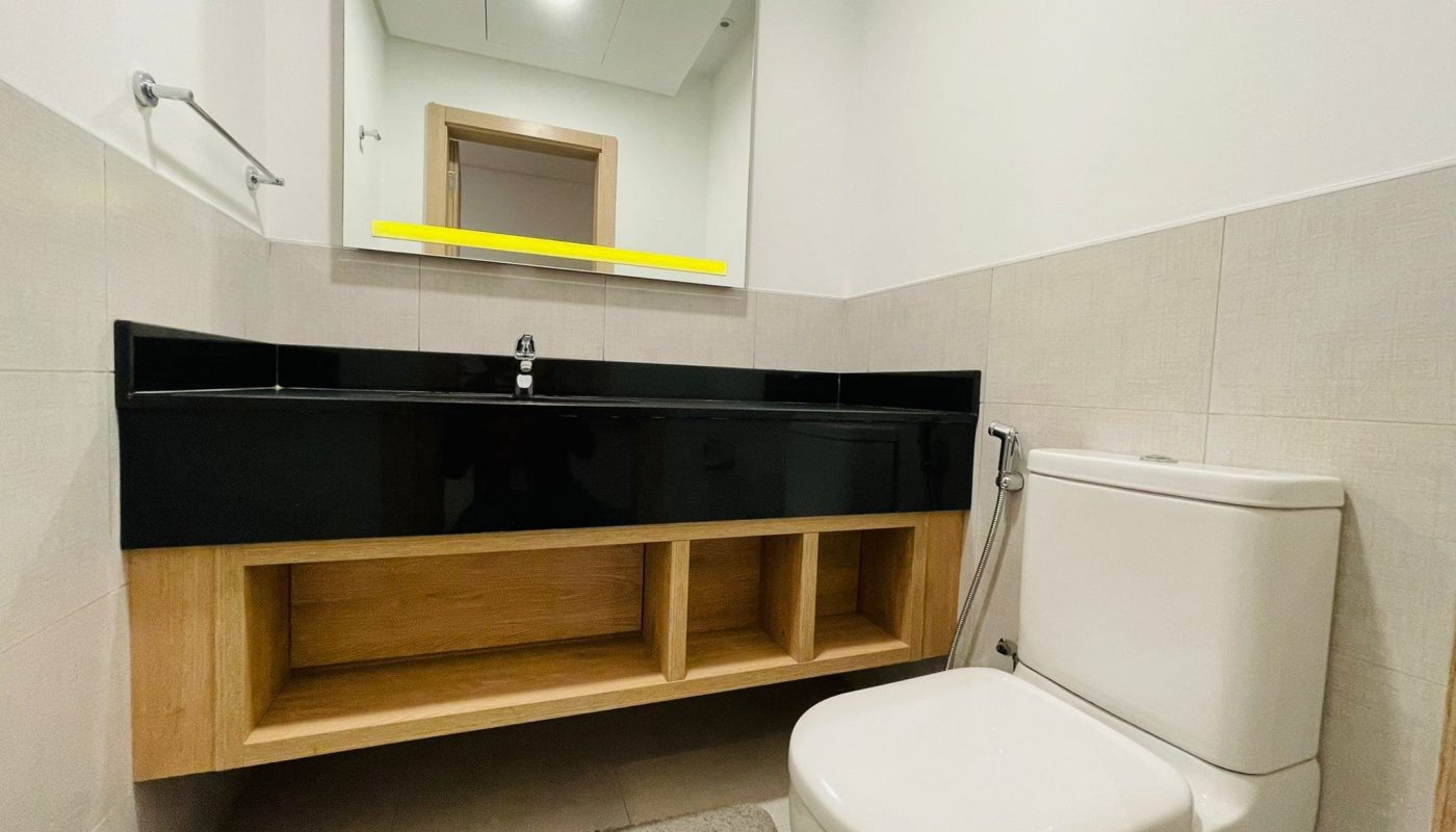 Luxury modern bathroom interior with a large mirror, black vanity, wooden shelf, and a white toilet in a 1 BR apartment in Juffair.