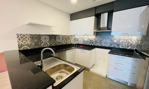 A modern kitchen in a luxury apartment with white cabinets, patterned backsplash, and stainless steel sink.