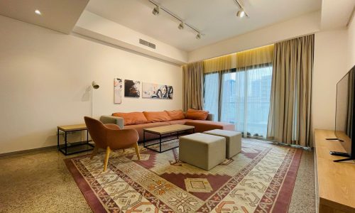 Spacious living room in a 1 BR luxury apartment with a modern sofa set, patterned rug, and abstract wall art.