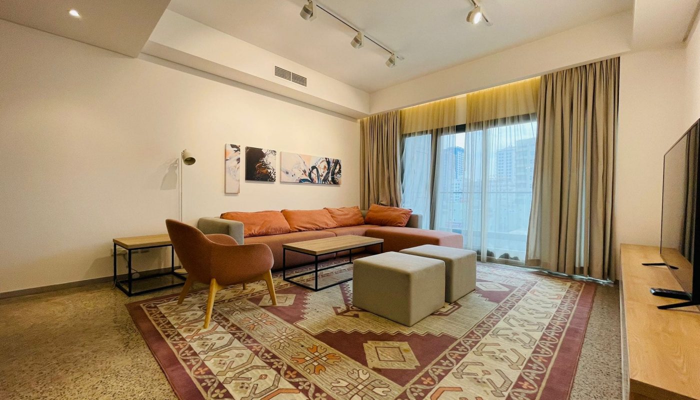 Spacious living room in a 1 BR luxury apartment with a modern sofa set, patterned rug, and abstract wall art.