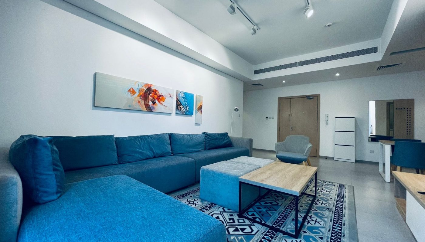 Modern living room with a blue sectional sofa, a geometric rug, and an auto draft colorful wall art piece.